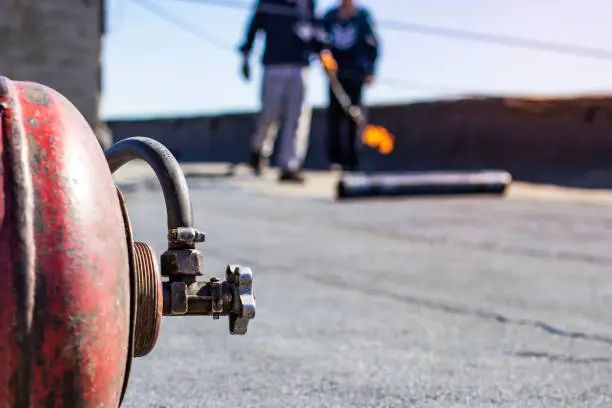 Photo of repair of bitumen roof with roll surfacing material with fire gas burner close-up, front and background blurred with bokeh effect