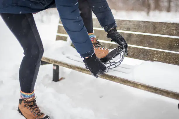 woman getting ready to take hike in snow fixing cleat onto boots