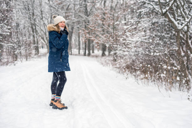 portrait of active middle aged woman hiking in snowy winter forest happy woman walking on forest trail in winter with light snow falling snow hiking stock pictures, royalty-free photos & images