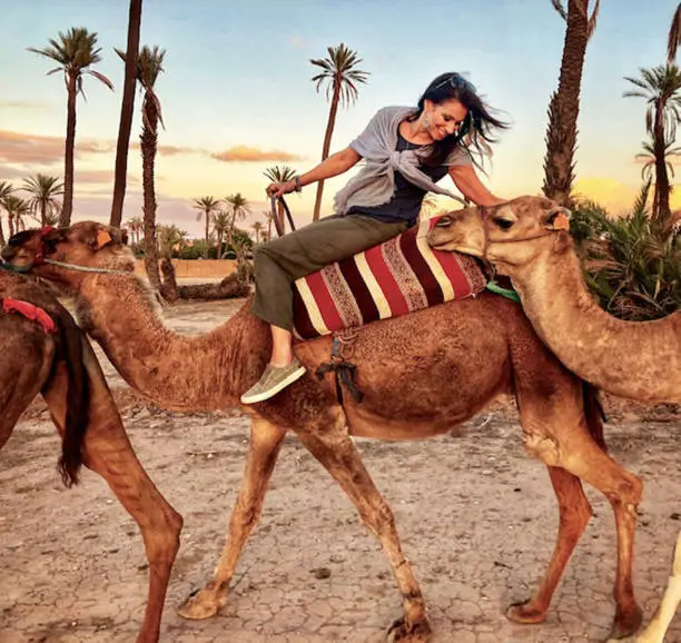 A happy, smiling woman rides a camel in a desert at sunset near Marrakech, Morocco