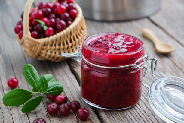 vasetto di mirtilli rossi schiacciati per salsa o marmellata e cesto di bacche di palude sullo sfondo. - cranberry juice foto e immagini stock