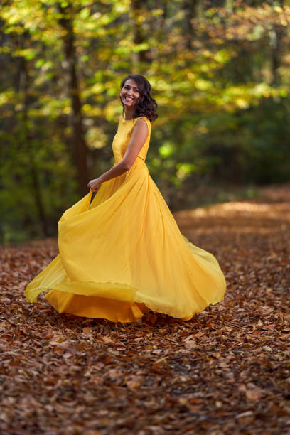 Happy young woman in long yellow dress dancing in an autumn landscape