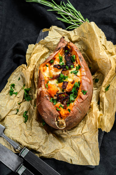 istock Baked sweet potato stuffed with cheese and bacon. Black background. Space for text 1188278909