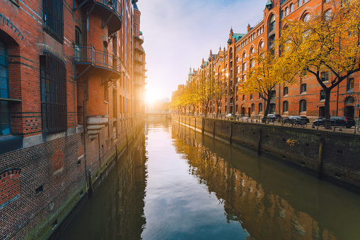 Speicherstadt warehouse district in Hamburg, Germany. Autumn season weather. Old brick buildings, river channel of Hafencity quarter with sunset golden flares and water reflections