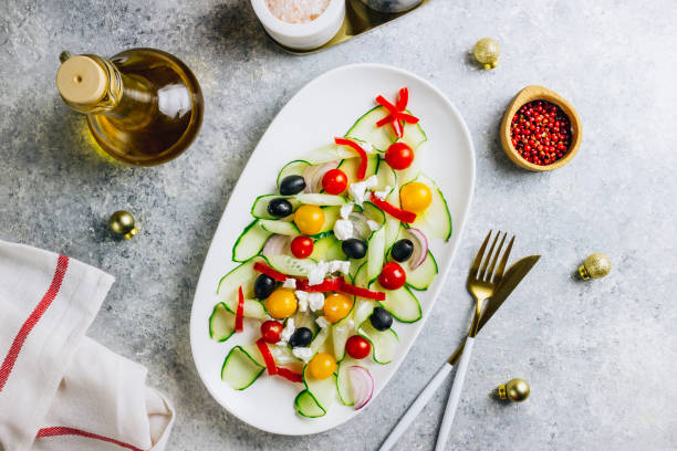 salade grecque de légumes aux tomates, fromage feta, oignons, concombre et olives. forme d'arbre de noel. servi sur une assiette blanche sur la table de fête. vue du haut. flat lay. espace de copie - christmas lunch mediterranean cuisine color image photos et images de collection