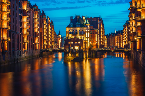 Hamburg city old port in blue hour, Germany, Europe. Historical famous warehouse district with illuminated water castle palace mirrored in river.