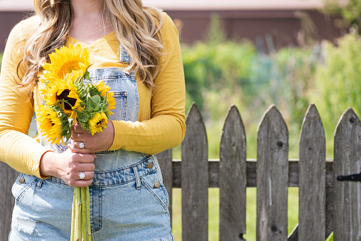 young woman in overalls holding sunflowers in garden