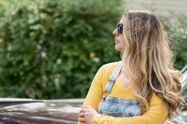 confident young woman wearing sunglasses and jean overalls - fashion women denim farm imagens e fotografias de stock