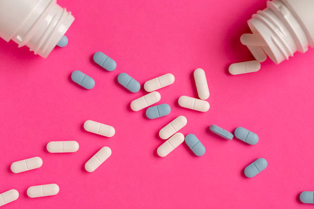istock White pill bottles on a pink background and scattered white and blue tablets 1188288999
