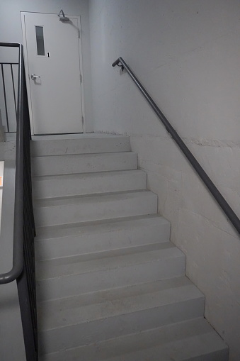 Stairs going up to door,throough a natural lit dingy grey fire emergency stairwell  in a building