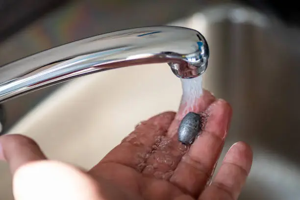 Person holding lead metal in water flow from tap