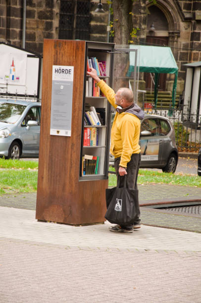 transeunte que olha para pedir um livro de uma prateleira de livro livre da comunidade em dortmund hoerde em alemanha - men reading outdoors book - fotografias e filmes do acervo