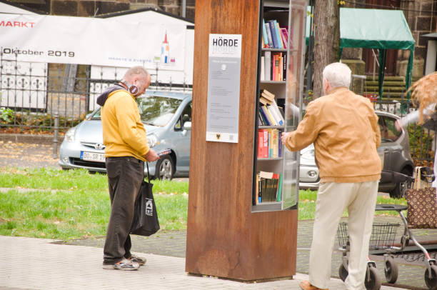 homem idoso que olha para pedir um livro de uma prateleira de livro livre da comunidade em dortmund hoerde em alemanha - men reading outdoors book - fotografias e filmes do acervo