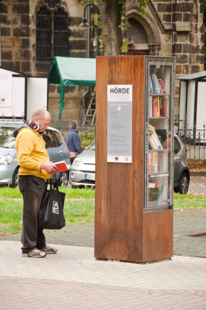 homem idoso que olha para pedir um livro de uma prateleira de livro livre da comunidade em dortmund hoerde em alemanha - men reading outdoors book - fotografias e filmes do acervo