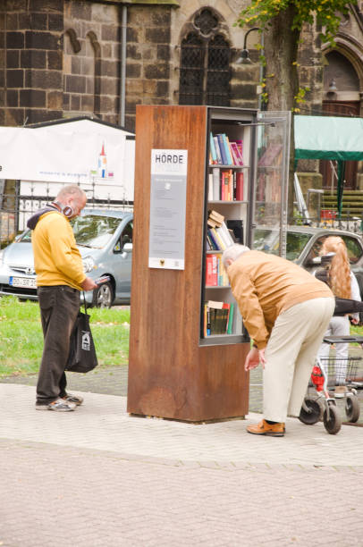 homem idoso que olha para pedir um livro de uma prateleira de livro livre da comunidade em dortmund hoerde em alemanha - men reading outdoors book - fotografias e filmes do acervo