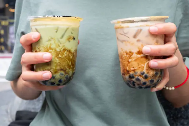 Photo of Cropped shot of woman holding a couple cup of iced Bubble tea (Milk tea and Green tea) in her hands.