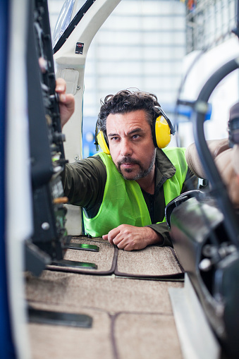 Man of Latin ethnicity aged 20-30 years who is a helicopter technician is checking a helicopter