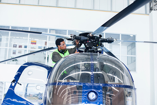 Brown-skinned man of Latin ethnicity aged 20-30 years who is a helicopter technician is checking a helicopter