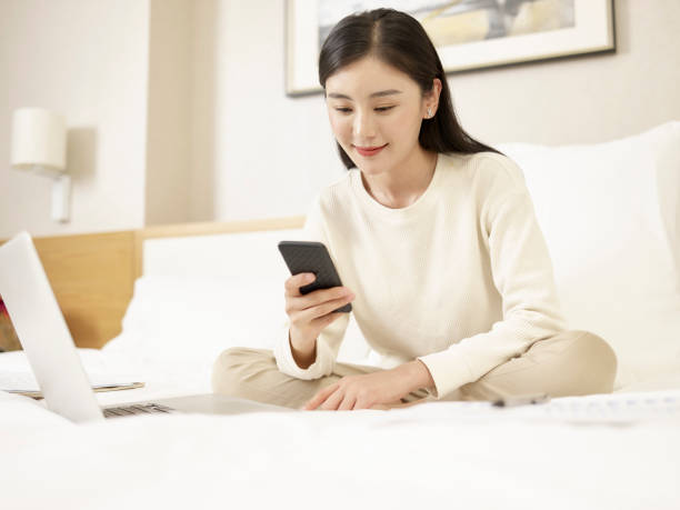 istock young asian woman using cellphone and laptop on bed 1188333716