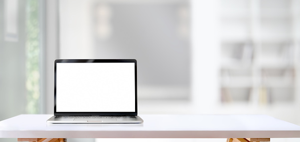 Open blank screen laptop computer on white wooden table with living room in the background