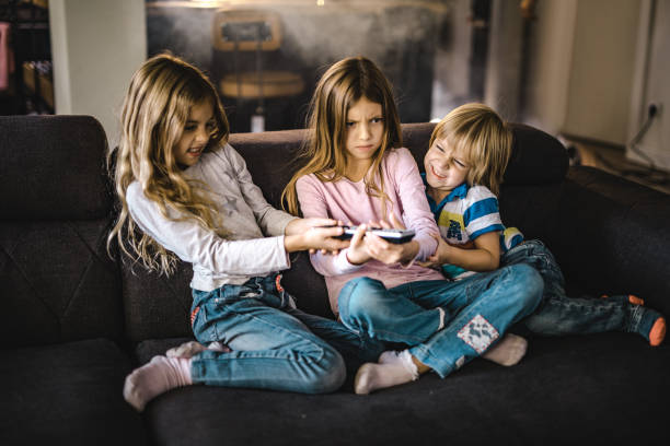 Small siblings fighting over a remote control in the living room. Angry little kids fighting over a remote control while watching TV on sofa at home. sibling stock pictures, royalty-free photos & images
