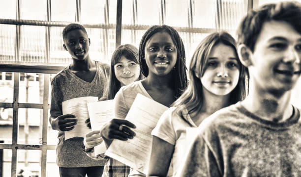 istock Group of multi ethnic students standing in line giving their work to teacher 1188354003