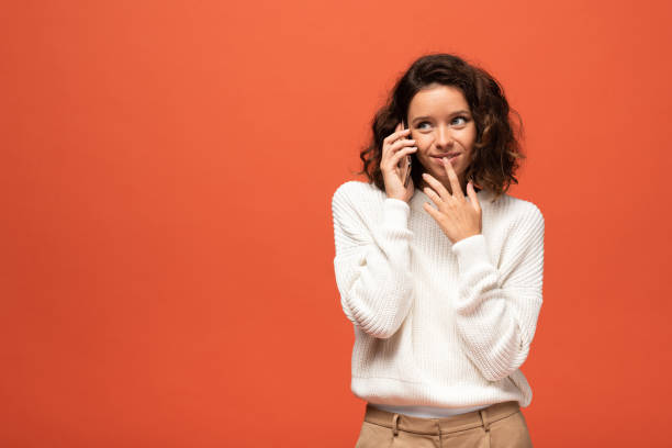 istock smiling curly woman talking on smartphone isolated on orange 1188355498