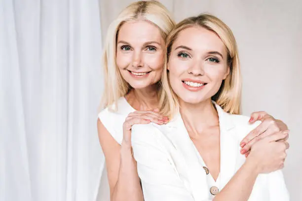 happy elegant blonde mother and daughter in total white outfits