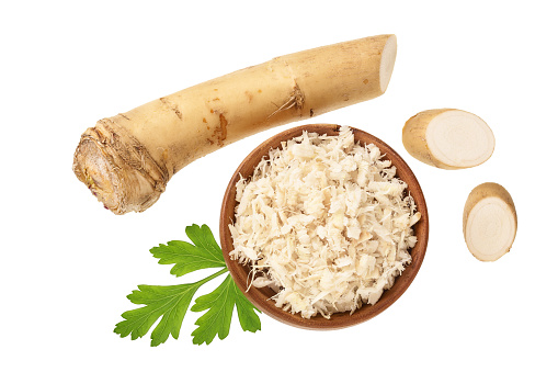 Horseradish root grated in wooden bowl with slices isolated on white background. Top view. Flat lay.