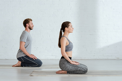 side view of young man and woman practicing yoga in thunderbolt pose
