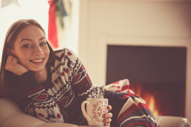 istock Cheerful young woman looking at camera while relaxing by the fireplace and enjoying tea 1188368429