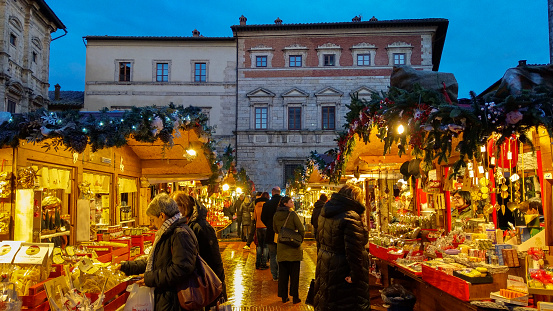 Montepulciano, Italy - November 17, 2019: Montepulciano at Christmas is transformed into a Christmas market (free admission) with over sixty wooden houses where you'll find handicrafts, delicatessen products, decorations and gifts. Inside the Castle of Montepulciano, instead, children can enjoy the Christmas village set up just for them. In this photo there are many happy people making shopping at the christmas market in the main square of Montepulciano medieval town, Tuscany, Italy