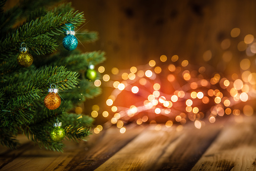 Fir tree decorated with Christmas balls on wooden floor against defocused background