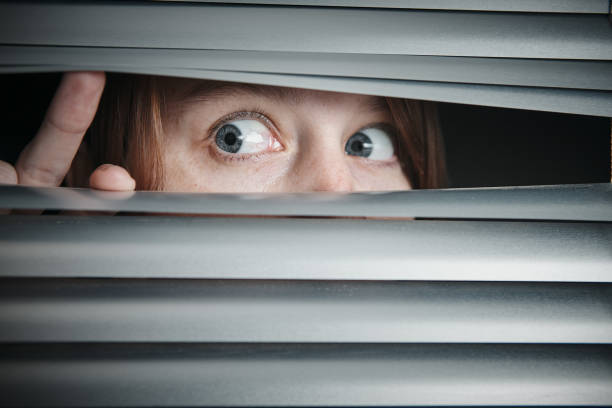 istock Scared young woman peeping sideways through blinds 1188370793