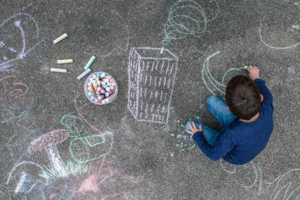 young boy drawing on the sidewalk with chalk - child chalking imagens e fotografias de stock