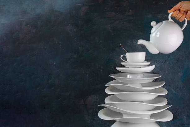Christmas tree made with white dishes with tea cup on topand teapot in hand over it. Creative concept about dishware, kitchen, restaurant, cafe, postcard, manufacture of plate, tableware. Horizontal