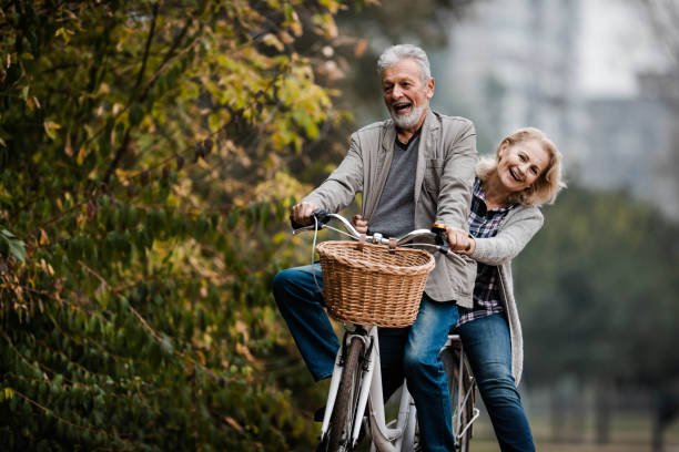 秋の日に自転車で楽しむ遊び心のあるシニアカップル。 - senior adult fun autumn senior couple ストックフォトと画像