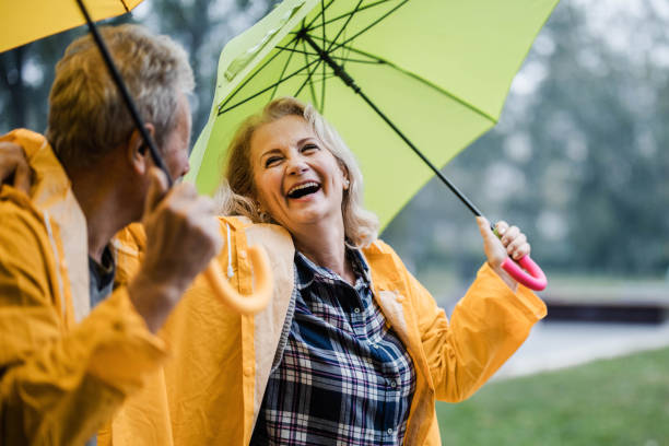 couples mûrs joyeux dans les imperméables jaunes parlant sous des parapluies. - umbrella senior adult couple autumn photos et images de collection