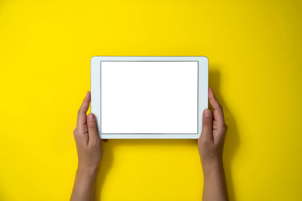 Hands holding digital tablet on yellow background stock photo