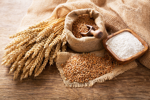 wheat ears, grains and bowl of flour on a wooden table, top view