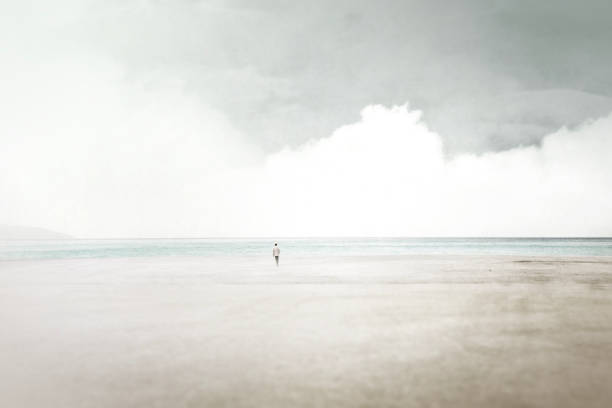 minimal surreal landscape, man walking on the beach beside the calm sea stock photo