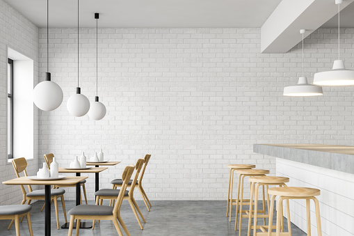 Side view of stylish minimalistic loft style pub with white brick walls, concrete floor, long white bar stand with stools and square tables with chairs. 3d rendering