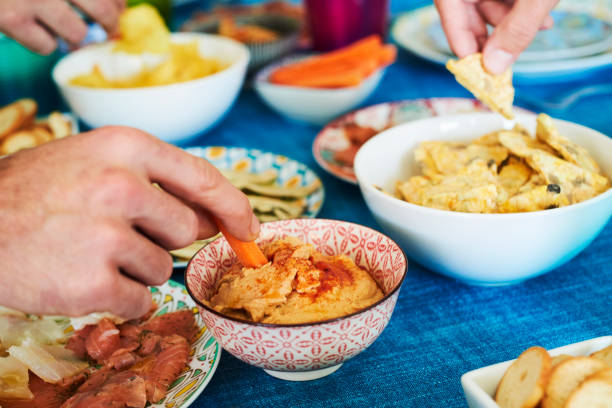 people having some appetizers on a colorful table some people having some different appetizers, such as hummus, potato chips and salmon and cod carpaccio, served on different colorful plates and bowls placed on a table set with a blue tablecloth dipping photos stock pictures, royalty-free photos & images