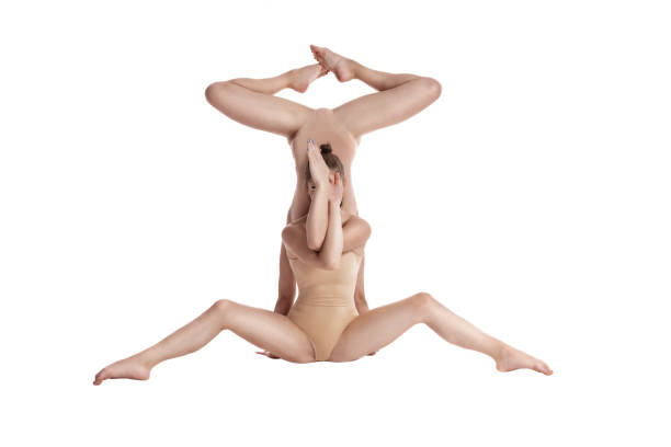 Two flexible girls gymnasts in beige leotards performing complex elements of gymnastics using support, posing isolated on white background. Close-up Two professional girls gymnasts in beige leotards performing complex elements of gymnastics upside down, using support, posing isolated on white. Concept of sports, healthy lifestyle. Close-up. leotard stock pictures, royalty-free photos & images