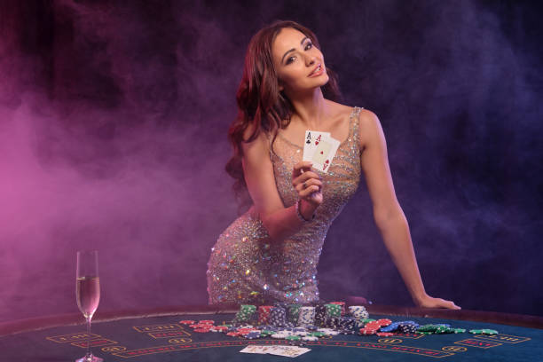 Girl playing poker, casino. Showing cards, posing at table with stacks of chips and money. Black, smoke background, colorful backlights. Close-up stock photo