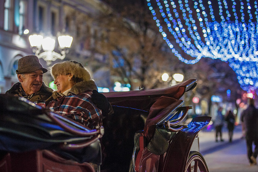 Copy space shot of affectionate senior couple relaxing together while sitting in a chariot and going on a romantic ride through beautifully decorated city street at Christmas time.