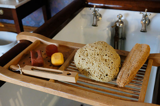 Old-fashioned Victorian bath tray containing a natural sponge, luffa, soap and a wooden thermometer