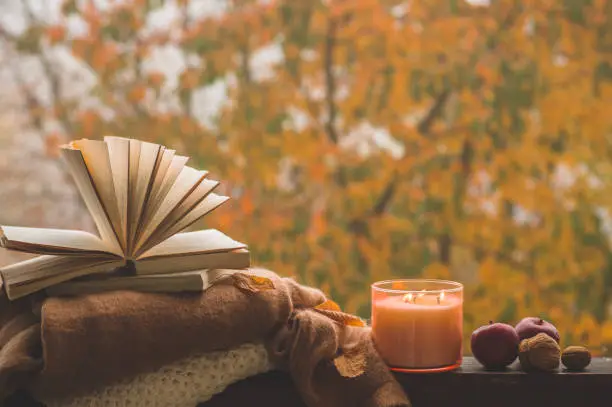 Photo of Still life details in home on a wooden window. Sweaters and candle,  autumn decor on the books. Read, Rest. Cozy autumn or winter concept.