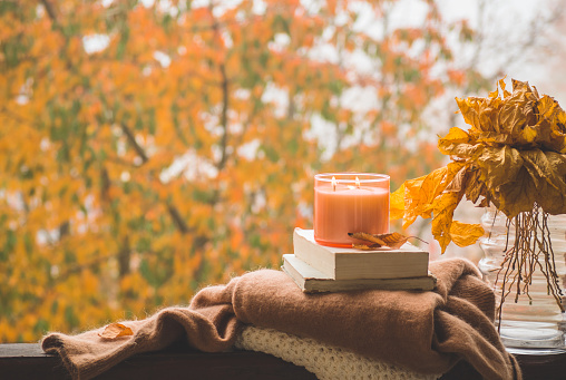 Sweet Home. Still life details in home on a wooden window. Sweaters and candle,  autumn decor on the books. Read, Rest. Cozy autumn or winter concept.