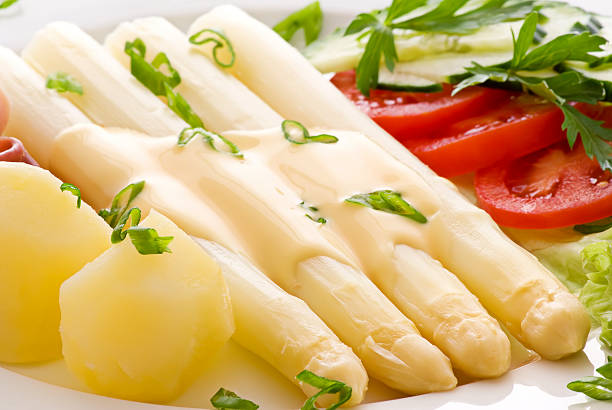 Yellow asparagus covered with sauce served with ham White asparagus with hamm potatos and fresh vegetables on a white plate. hollandaise sauce stock pictures, royalty-free photos & images